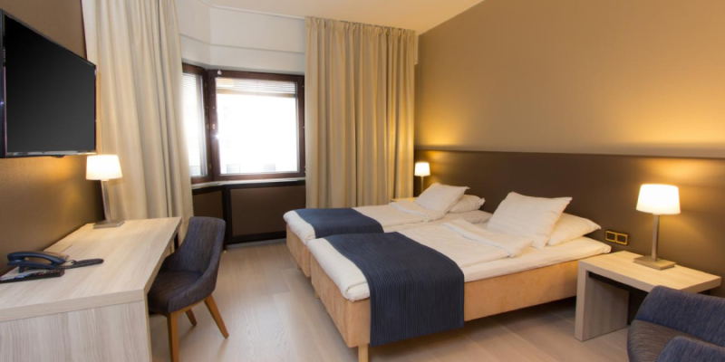 Kuva Hotel Oscarin huoneesta, jossa vaalea sisustus. Kuvassa parisänky ja työpiste 