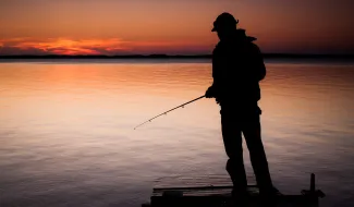Kalastaja seisoo laiturilla auringonlaskussa