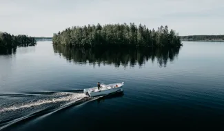 Moottorivene ajaa Saimaalla, kyydissä yksi henkilö pelastusliiveissä, taustalla saari