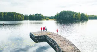 Ilmakuva Taipaleen kanavalta, jossa kolme naista seisoo selin kameraan kanavan reunalla vesistöön katsoen