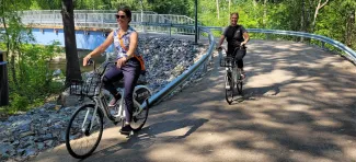 Kaksi naista pyöräilee valkoisilla kaupunkipyörillä Kämärillä