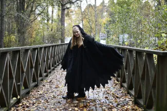 Mustaviittainen hahmo seisoo sillalla, jolla on keltaisia lehtiä.