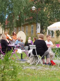 ihmisiä syömässä pihalla vohveleita ja kuuntelemassa rumpujen soittoa taustalla keltaisia puutaloja.