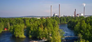 Ilmakuva Ämmäkoskelta ja kosken ylittävistä silloista. Vasemmalla näkyy punainen rakennus veden äärellä, taustalla tehtaan piiput. Sillalla pyöräilijä. 