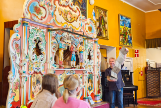 Mieshenkilö esittelee suurta Mekaanisen musiikin museon soitinta yleisölle