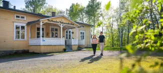 Keltainen kotiseutukeskuksen rakennus, jonka etualalla kävelee pariskunta